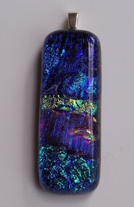 Various colors of dichroic glass layered over a black base. 3/4" wide by 1 7/8" long (excluding silver bail)